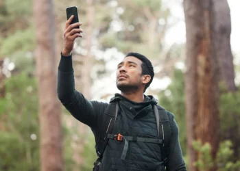 Homem com expressão de tensão tenta encontrar sinal de telefone em meio a um local desértico.