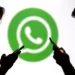 Um homem e uma mulher usam seus celulares simultaneamente. Há um logo do WhatsApp ao fundo, levemente desfocado. Falando sobre como fazer itálico no whatsapp.