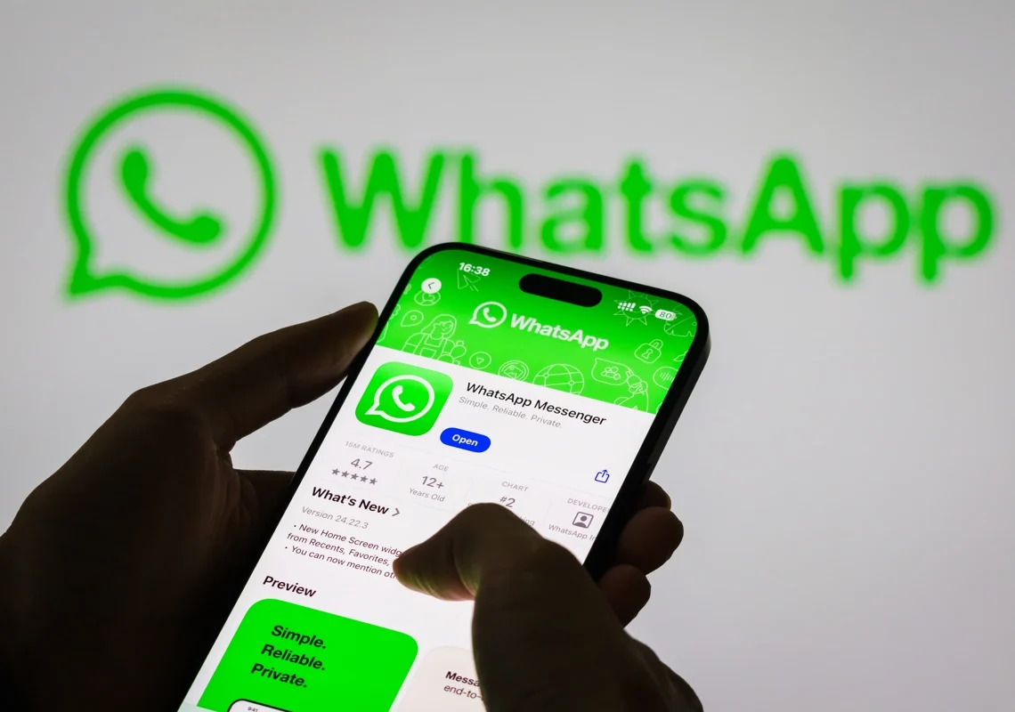 Pessoa segura smartphone que contém uma página de download para o WhatsApp. Ao fundo, o logo do app na parede. Ensinando como sublinhar no whatsapp.
