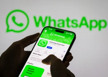 Pessoa segura smartphone que contém uma página de download para o WhatsApp. Ao fundo, o logo do app na parede. Ensinando como sublinhar no whatsapp.