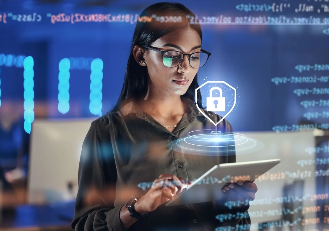 Mulher utiliza um tablet. A sua volta existem objetos adicionados digitalmente, incluindo um balão em forma de escudo com um cadeado dentro bem à sua frente. Falando sobre meios de comunicação na internet seguros.​