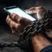 Mãos acorrentadas segurando um celular. Falando sobre vício em celular.